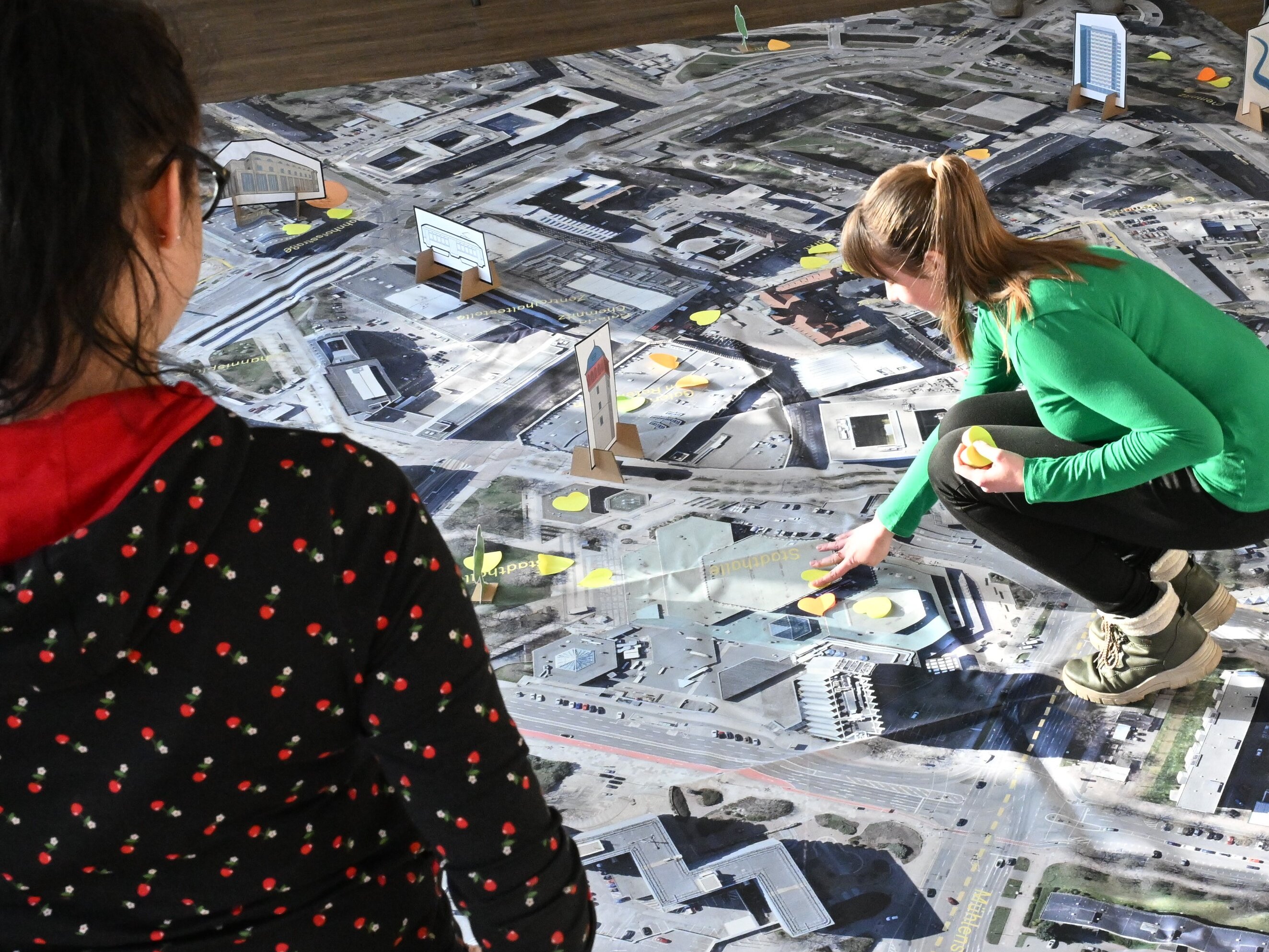 Eine junge Frau markiert auf einer großen Innenstadtkarte ihre Lieblingsorte mit Klebepunkten